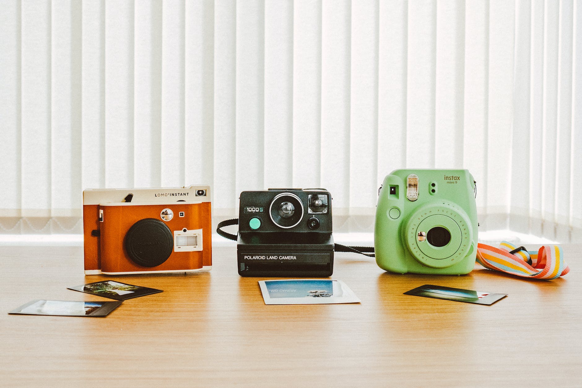 three assorted color instant cameras on the table with sample photos